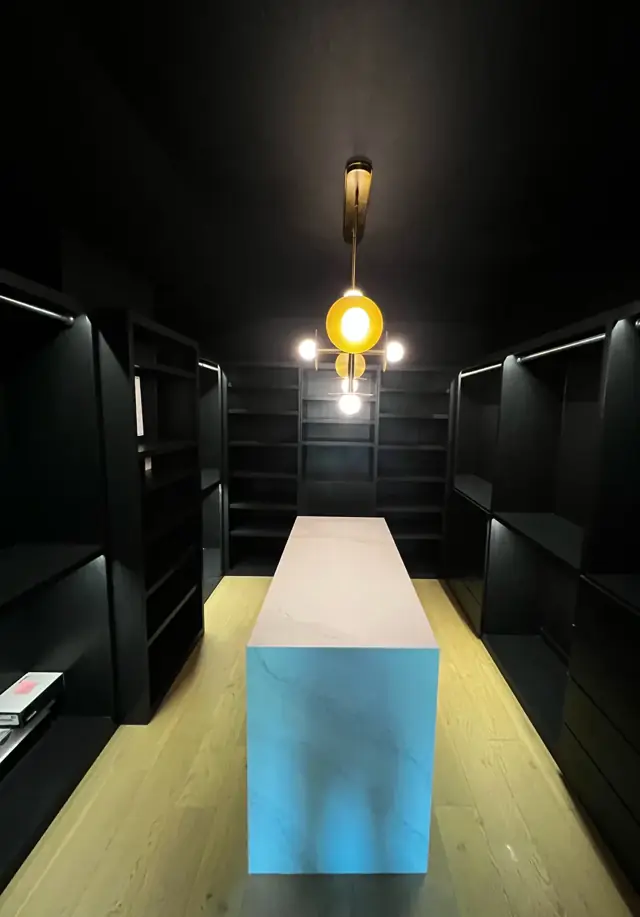 Dark walk-in closet with built-in shelving, center island, and pendant light