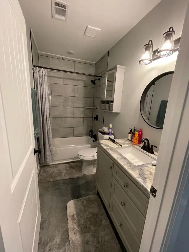 Bathroom with a round mirror, tiled shower, and vanity