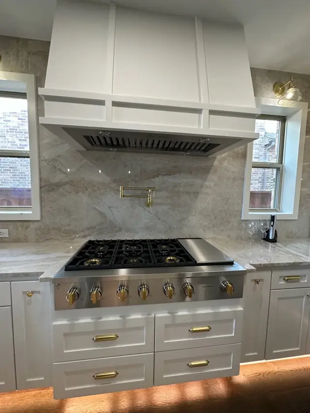 White kitchen with a pro range, plaster-style hood, and gold hardware