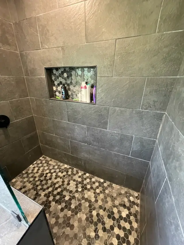 Dark slate-look tile shower with a pebble floor and niche