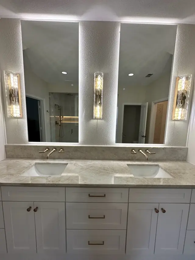Double vanity with backlit mirrors and wall sconces