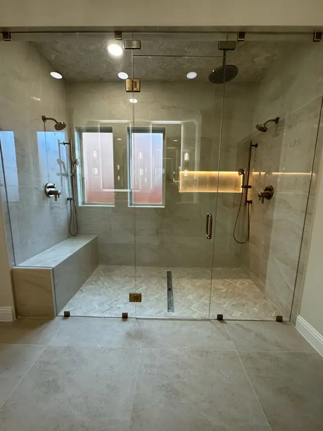 Large walk-in glass shower with a bench, rain head, and lit niche
