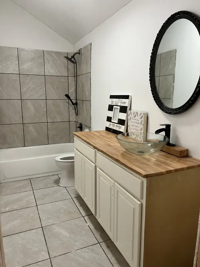 Bathroom with a wood-top vanity, round mirror, and tiled tub surround