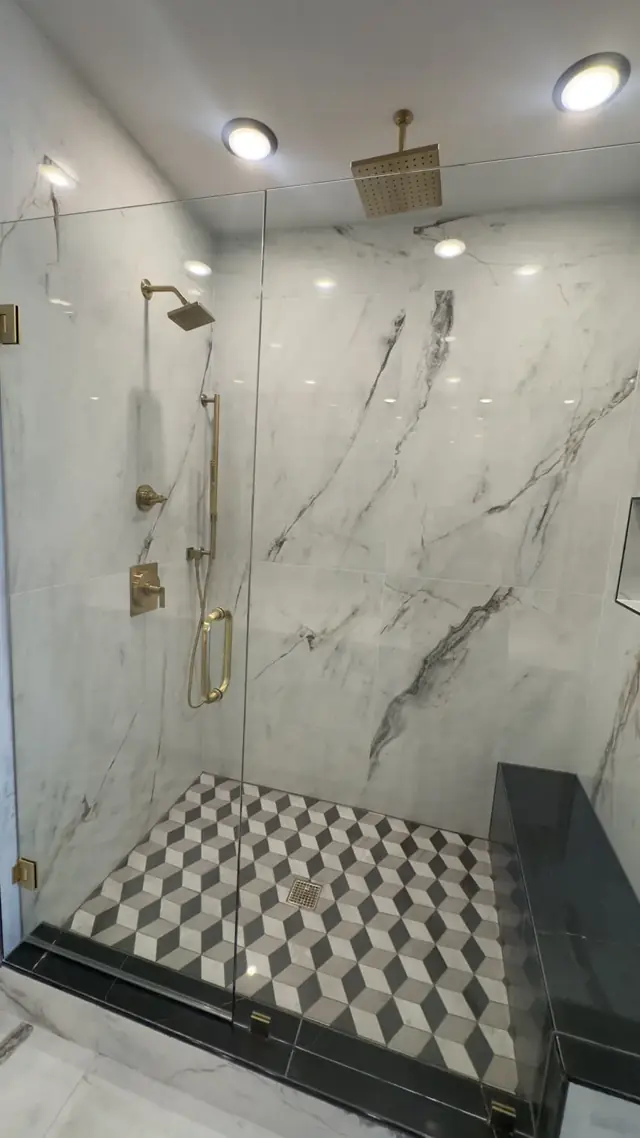 Marble-look walk-in shower with gold fixtures and a patterned floor