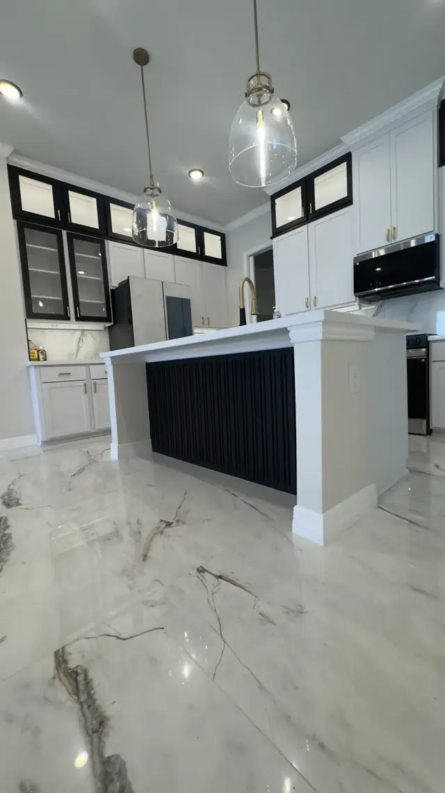 Kitchen island with a dark base, pendant light, and marble-look floors