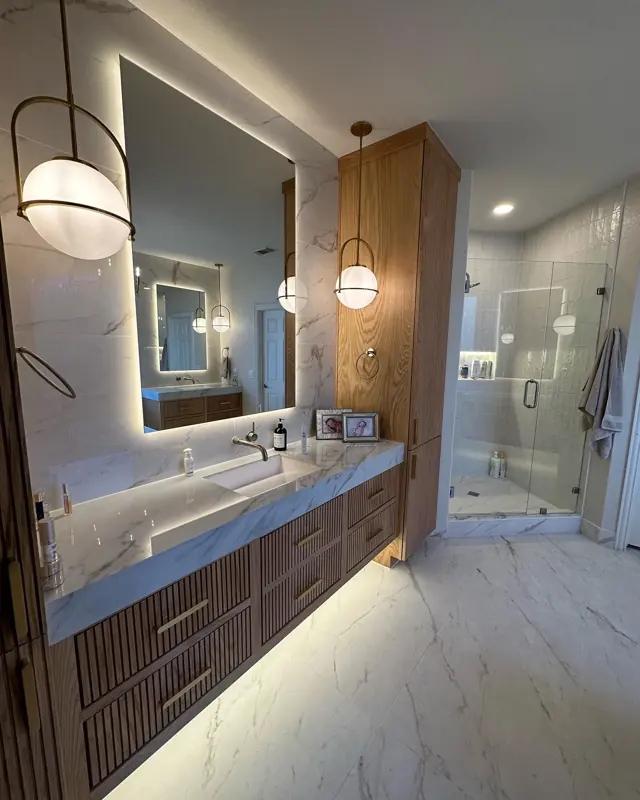 White-oak fluted floating vanity, marble-look slab, globe pendants, glass shower