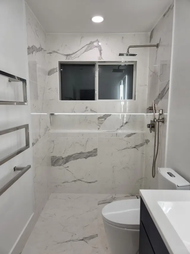 Marble-look walk-in shower with a lit niche
