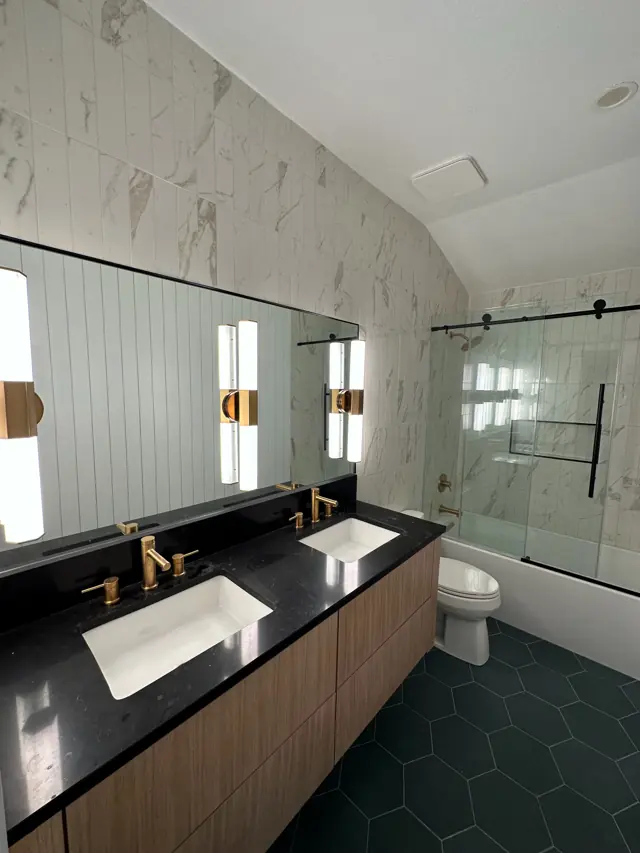 Bathroom with black counter, brass fixtures, oak vanity, and green hex floor tile